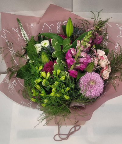 Mauve Garden Harmony - A lush and elegant bouquet showcasing soothing mauve and purple tones with touches of fresh green. This arrangement features a large lavender chrysanthemum, vibrant snapdragons, and deep plum blooms paired with delicate white flowers and unopened lilies for added sophistication. Textured greenery, including feathery foliage and variegated leaves, adds movement and fullness. Wrapped in soft mauve floral paper and presented in a matching gift bag, this bouquet exudes refined beauty—perfect for thoughtful occasions, anniversaries, or expressing heartfelt sentiments.